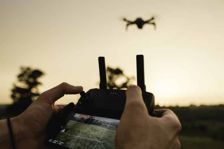 Pilote tenant sa radiocommande face à un drone en vol au coucher du soleil