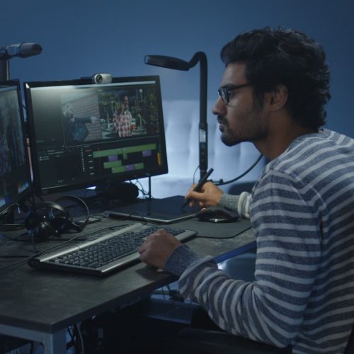 Monteur vidéo utilisant un stylet et une tablette graphique devant deux écrans d'étalonnage colorimétrique